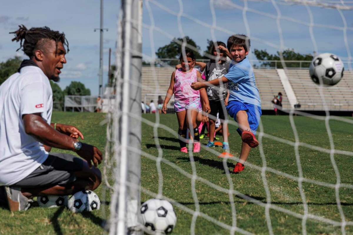 JJ Nunes, left, watches as a child kicks the ball into the net while running a drill with San Antonio FC players at a free soccer clinic at Honey Bowl Stadium in Uvalde, Texas, Thursday, Aug. 18, 2022. SAFC players and staff traveled to Uvalde to host the free clinic for young athletes, ages 4-15, from 4 to 6 p.m. on Thursday.