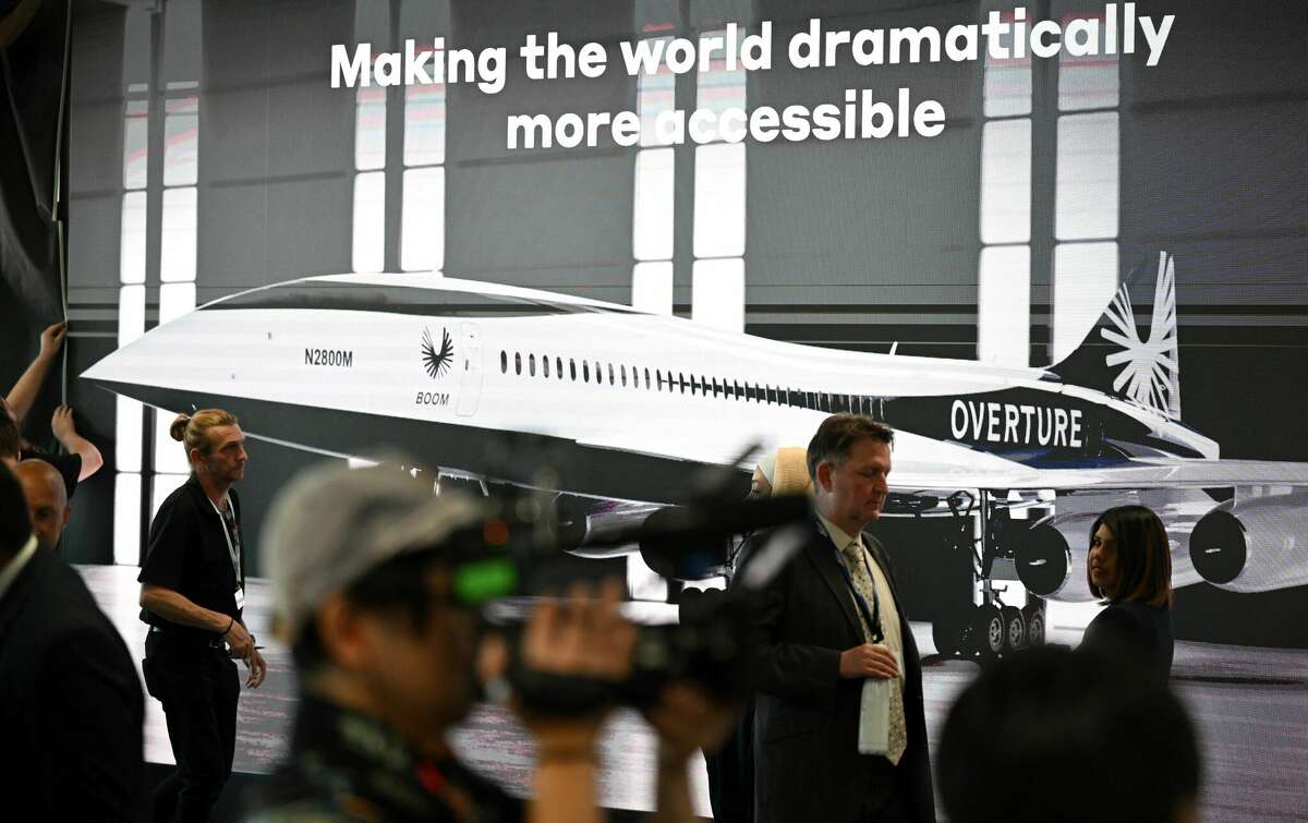 Attendees walk past a poster of a Boom Supersonic concept Overture aircraft at the Farnborough Airshow in July 2022.