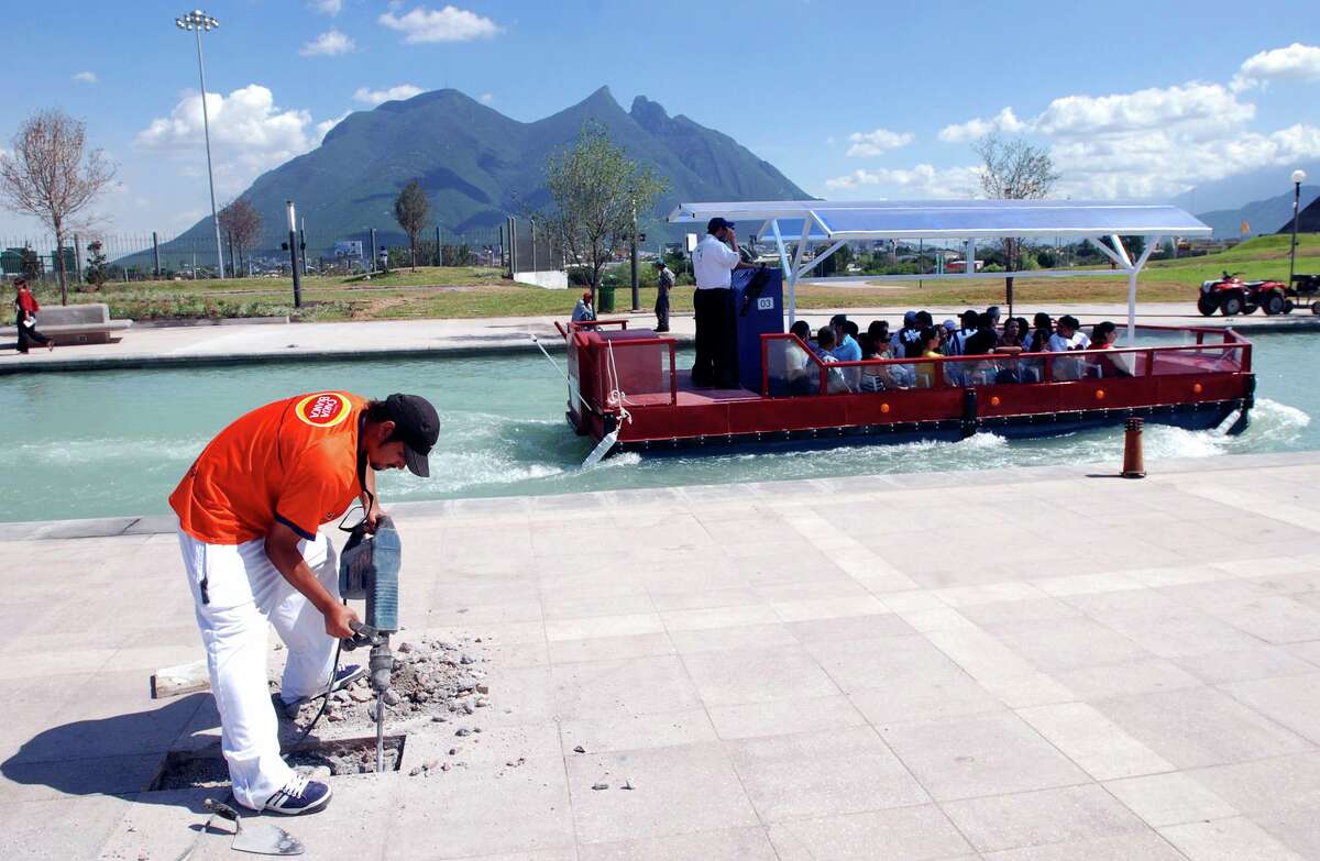 Un barco turístico hace una prueba con los visitantes por el Paseo Santa Lucía de Monterrey mientras un trabajador da el toque final a la atracción turística frente al emblemático Cerro de la Silla el jueves 27 de septiembre.