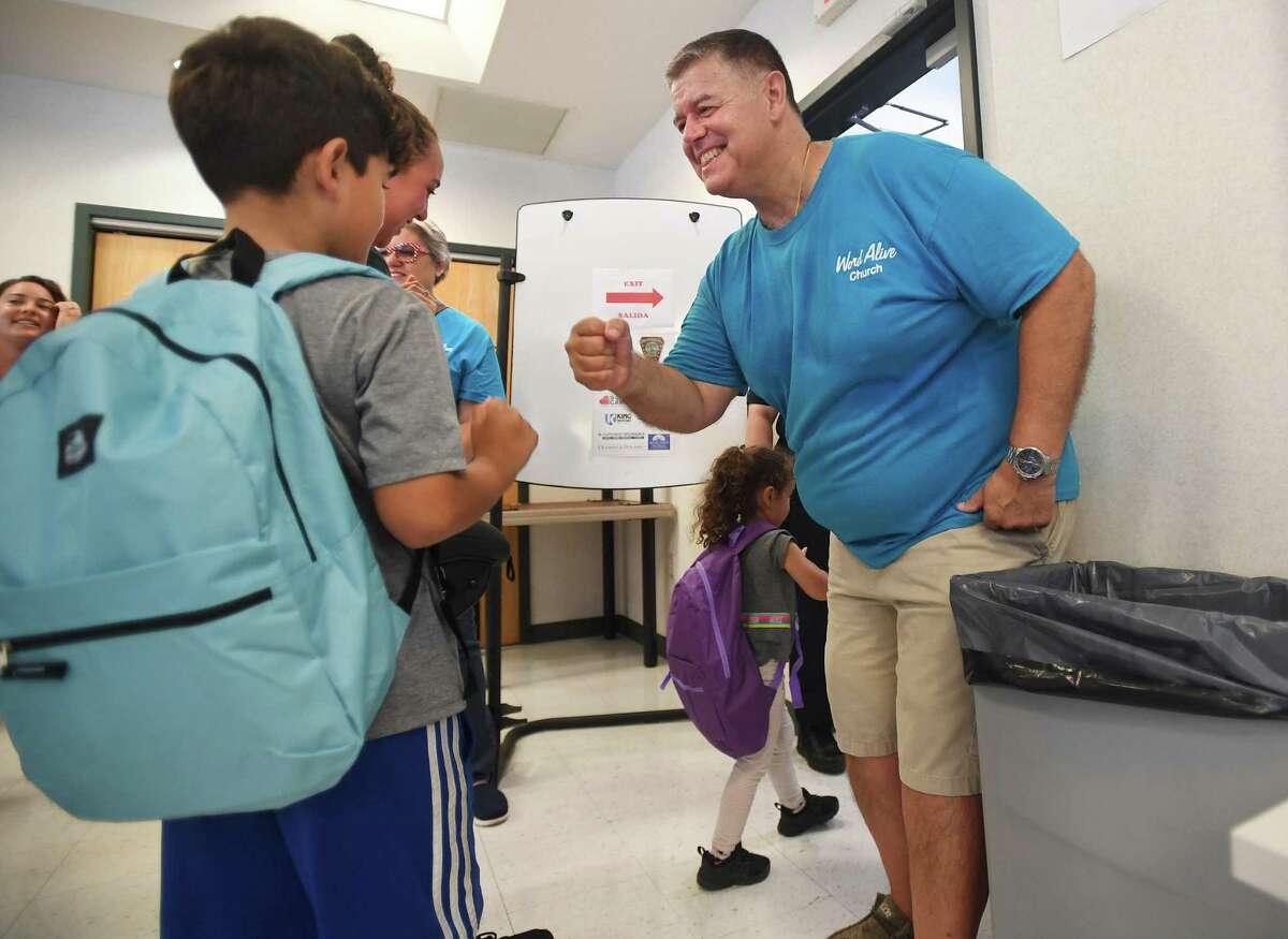Pastor Artie Kassimis of Word Alive Church fist bumps students after handing out new backpacks filled with school supplies at the Norwalk Police Department in Norwalk, Conn. on Saturday, August 20, 2022.