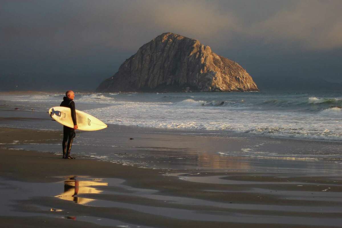 A surfer looks out at the Pacific Ocean near Morro Rock in Morro Bay (San Luis Obispo County).