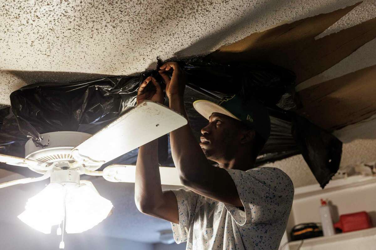 Yominique Hutchings pins a plastic bag over a hole in his living room ceiling in his one-bedroom unit at Vista del Rey Apartments in Leon Valley on June 16.