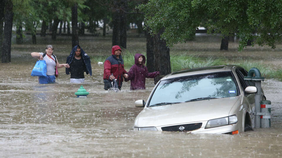 A group walk hand in hand through high water from their flooded apartment complex Monday, April 18, 2016, in Houston. ( Steve Gonzales / Houston Chronicle )