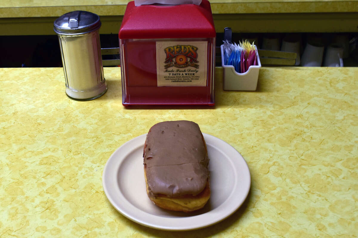 A maple bar injected with custard in the middle waits to be eaten on the signature Red's Donuts sunshine yellow counter.