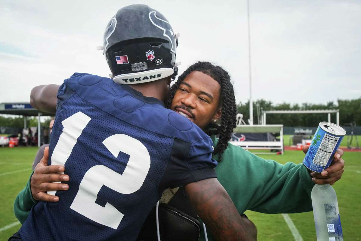 Texans rookie wide receiver John Metchie III embraces teammate Nico Collins (12) as he visits training camp Tuesday for the first time since his leukemia diagnosis.