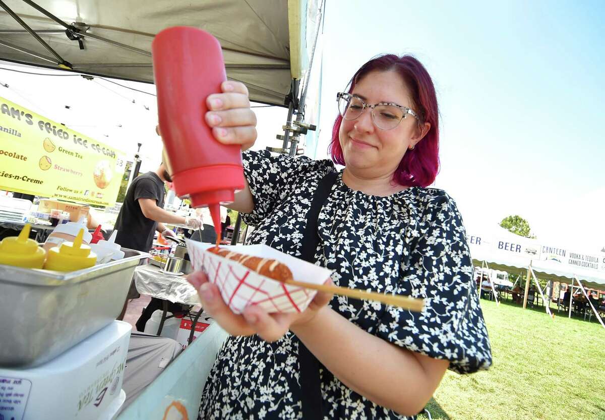 Sara Sapienza puts some ketchup on her corn dogs from Hangry Dog during the Hey Stamford! Food Festival at Mill River Park in Stamford, Conn., on Saturday August 20, 2022. Sunday is the final day of the festival at will feature Vanilla Ice, Rob Base and All For One as part of the I Love the 90's tour.