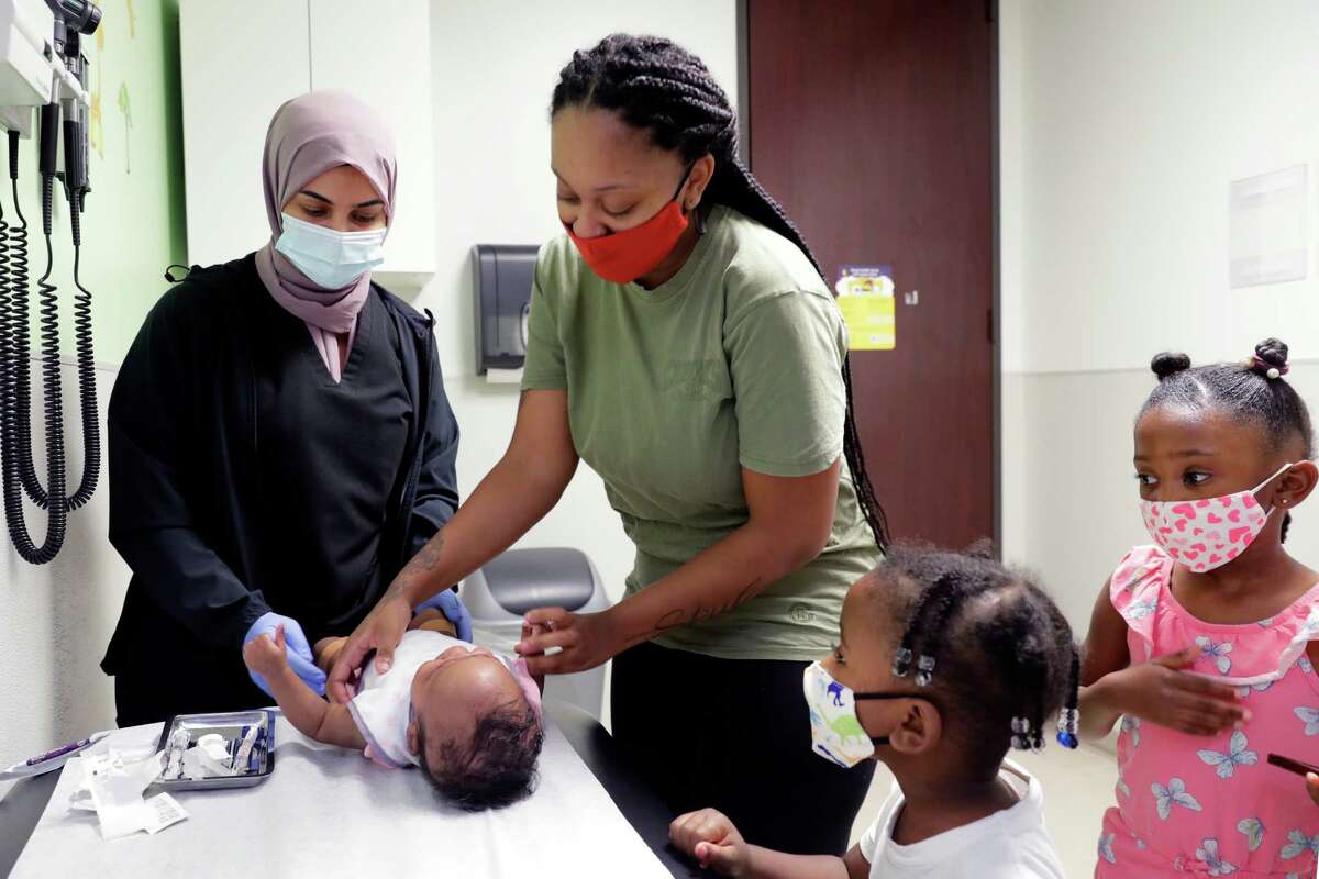 Nurse Wrood Hasan, left, administers immunization shots to 2-month-old Kh’Alani Stewart, bottom, as mom Keaunni Sampract, center, supports the child. Aiden Sampract, 4, and Skylar Sampract, 5, look on.