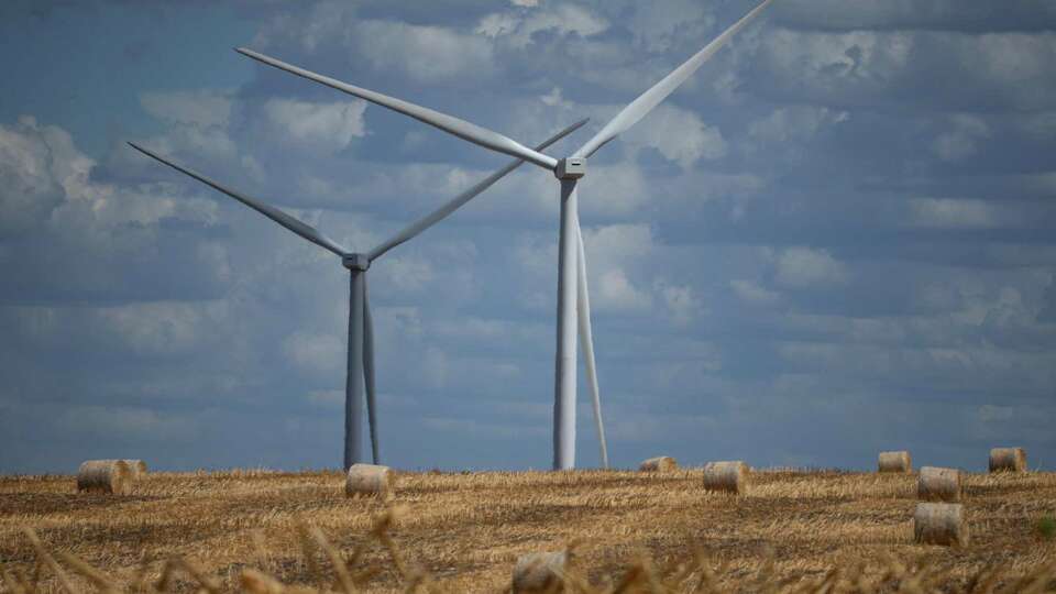 Wind turbines producing energy behind a field of hay barrels Tuesday, Aug. 9, 2022, in Mart. Engie, a French company whose North American hub is based in Houston, operates 100 turbines on more than 30,000 acres for the Prairie Hill Wind Project.