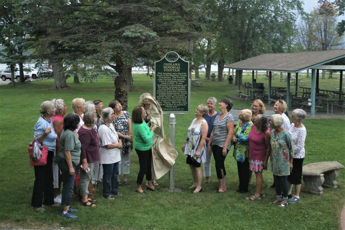 Shirley Brooks (center), of the Portage Lake Garden Club, unveils a Michigan historic marker installed at the Memorial Fountain in Onekama Village Park Thursday as other club members look on.