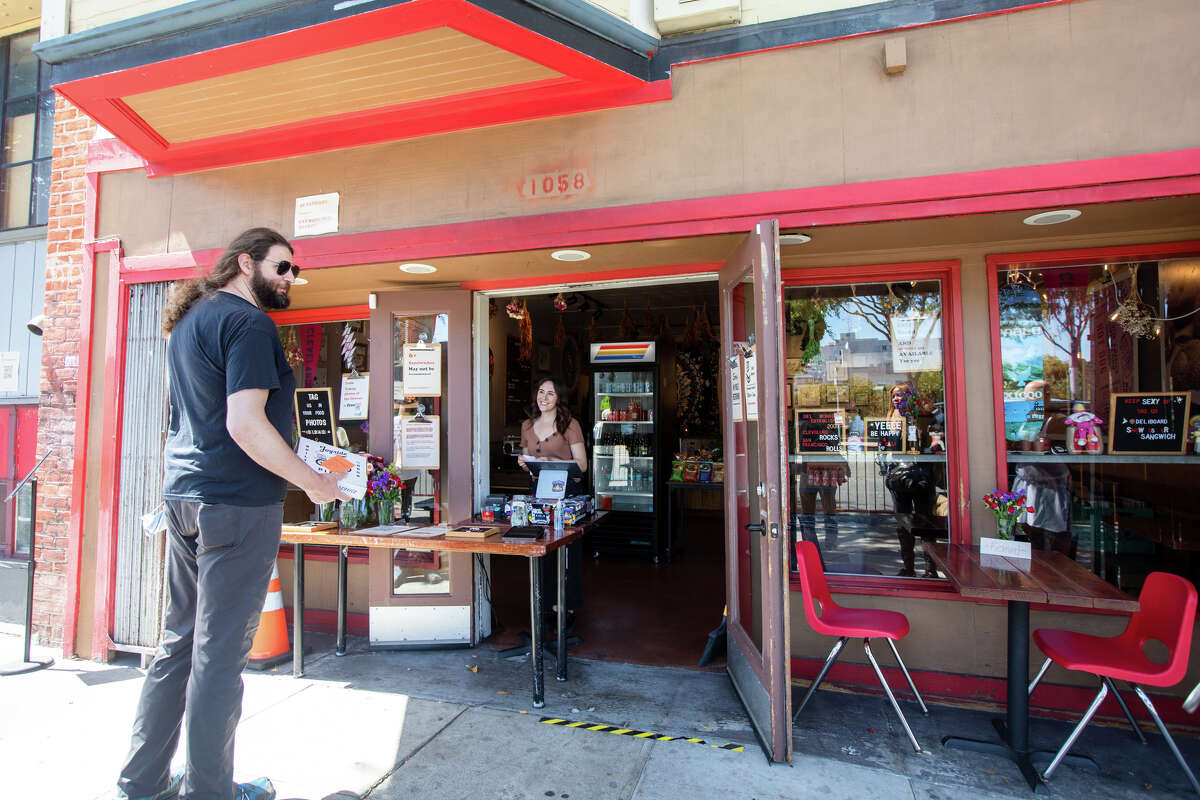 Employee Justice Stone takes orders from customers at the entryway of Deli Board in San Francisco, Calif. on Aug. 19, 2022. The deli used to have a dining room but the restaurant has been covered to take-out only since the start of the COVID-19 pandemic.