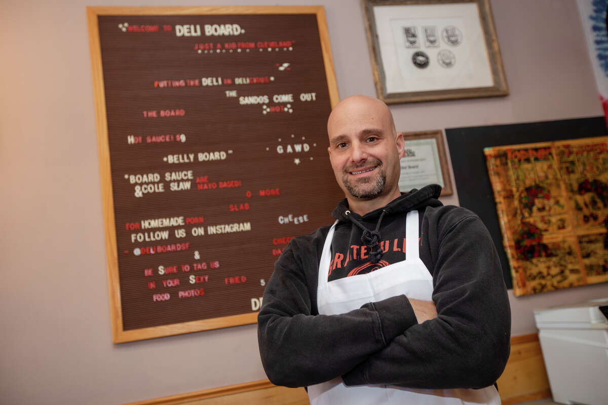 Adam Mesnick stands in front of a sign board inside his restaurant Deli Board in San Francisco, Calif. on Aug. 19, 2022.
