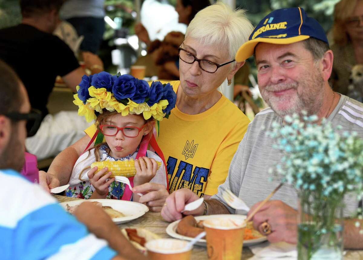 Hailey Shnitser, 5, of Bethel , wearing a Ukrainian wreath, made by her grandmother, eats her lunch with her grandparents, Tanya and Mark Shnitser, native Ukranians at Sunday’s Ukrainian Festival at the Castle Hill Farm in Newtown, August 28, 2022.
