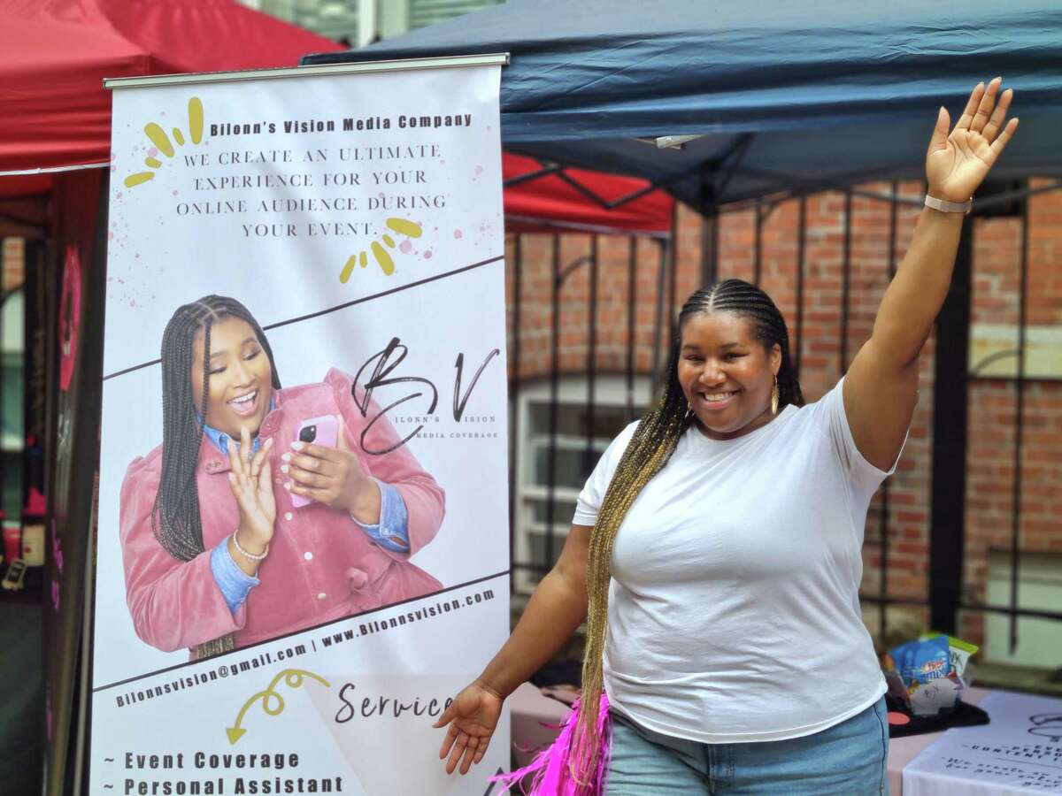 Sheena Postell poses in front of her poster promoting her social media business at Black Wall Street Festival at Temple Plaza in New Haven Aug. 27, 2022.