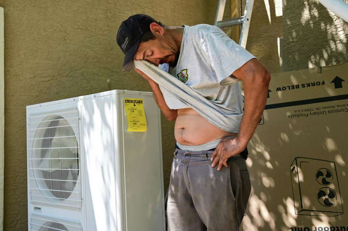 Evan Thompson, an installer with A 100% Guarantee Heating & AC, wipes sweat off of his face while installing a new electric AC unit in Vacaville, Calif. on Tuesday, Aug. 16, 2022. A heat wave was expected to bring a blast of hot weather, and triple-digit temperatures, to parts of the Bay Area. (Samantha Laurey/Special to SF Chronicle)