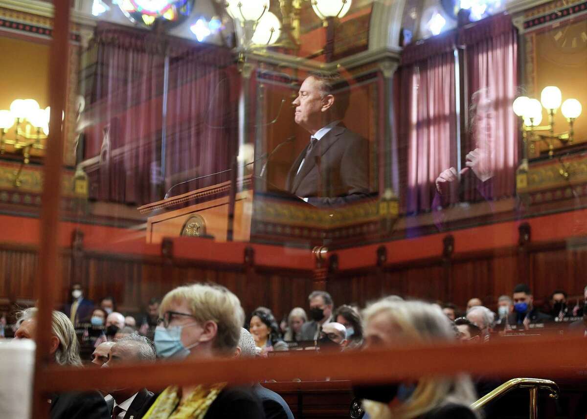 His image reflected in a protective screen, Governor Ned Lamont addresses the combined House and Senate during the opening day of the 2022 legislative session at the Capitol in Hartford, Conn. on Wednesday, February 9, 2022.