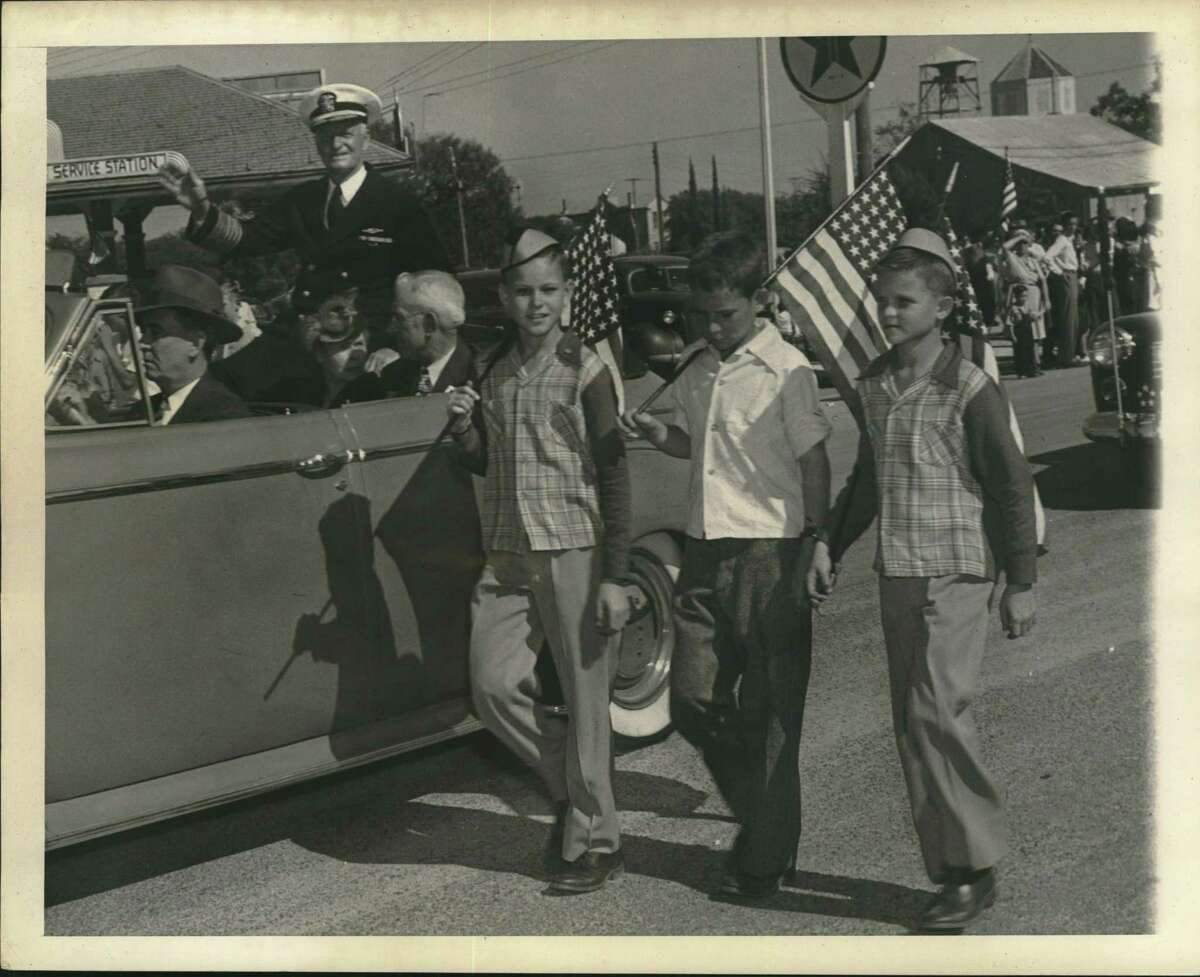 Three Fredericksburg, Texas youths, each carrying an American flag, march in a parade at Fredericksburg, Texas, October 3, 1945, by the side of the automobile carrying Fleet Admiral Chester W. Nimitz, who was visiting the city of his birth before returning to the Pacific.
