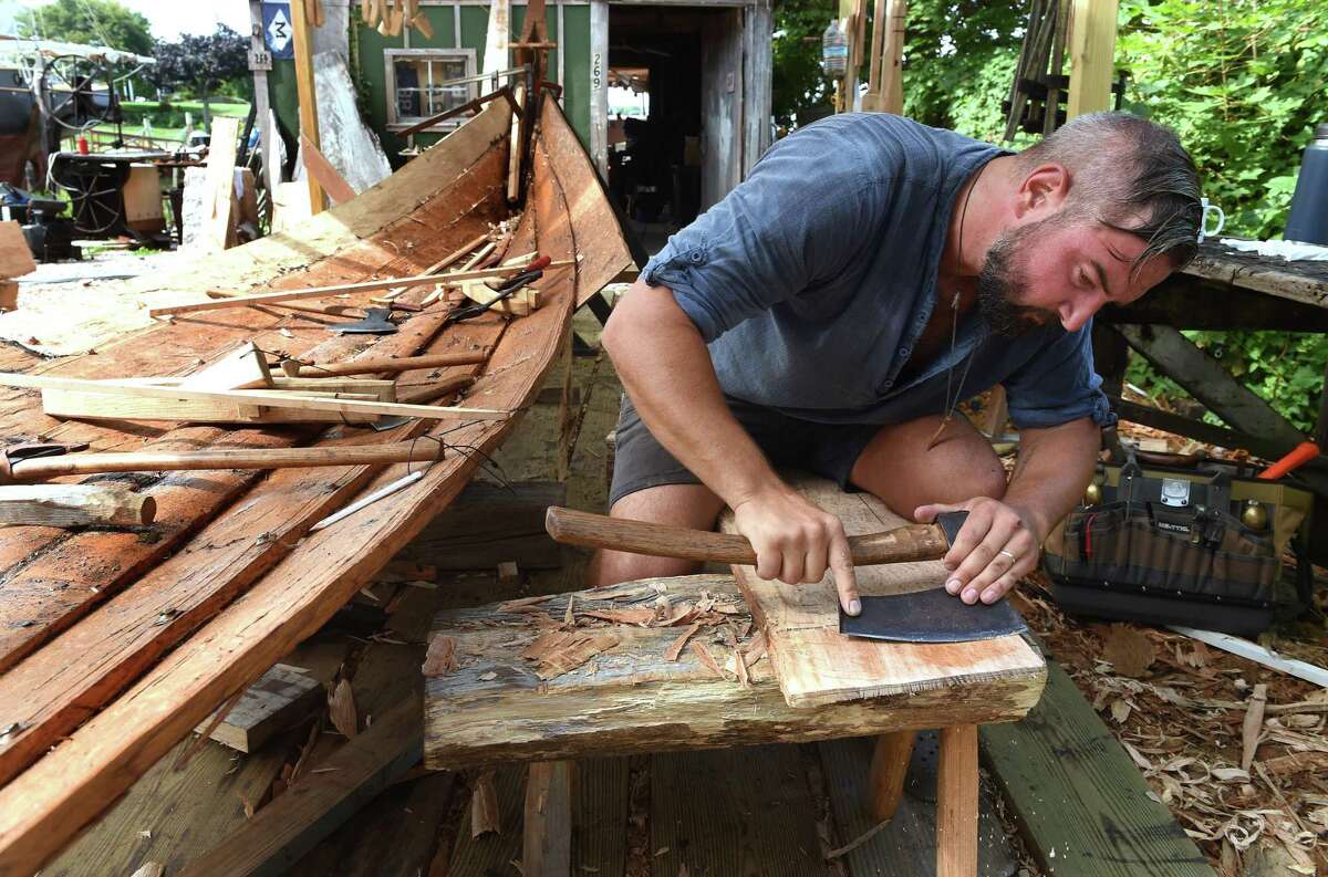 Matt Barnes of Leetes Island Boatworks hews the end of a plank of white oak with a broad axe in Stony Creek on August 23, 2022 for a replica of a Danish fishing vessel dating from 1130.