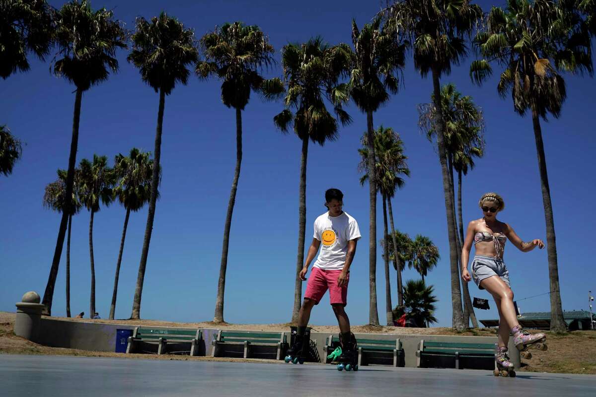 La gente patina bajo las palmeras en medio de temperaturas de tres dígitos en varias partes del sur de California el miércoles en la sección de Venice Beach en Los Ángeles.