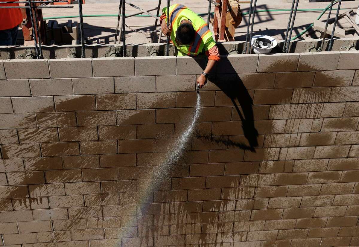 随着气温上升，一名建筑工人在安提阿海水淡化厂现场向一堵墙喷水。