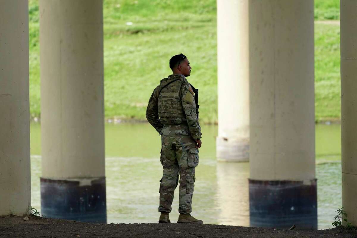 A member of the Texas National Guard looks across the Rio Grande to Mexico from the U.S. at Eagle Pass, Texas, Friday, Aug. 26, 2022. The area has become entangled in a turf war between the Biden administration and Texas Gov. Greg Abbott over how to police the U.S. border with Mexico.