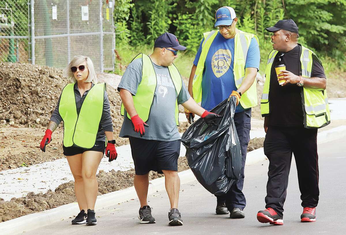 John Badman|The Telegraph Alton Mayor David Goins holds open a trash bag for one of about a dozen workers and volunteers who joined him to pick up trash along Rock Spring Drive between College Avenue and Brown Street Friday morning. The group met at Rock Spring Park and walked the stretch which has had numerous recent improvements, including a new sidewalk for children walking to Alton Middle School. Alton’s Fall City-Wide Litter Clean-Up is planned 9 a.m. to noon on Saturday, Sept. 10. 