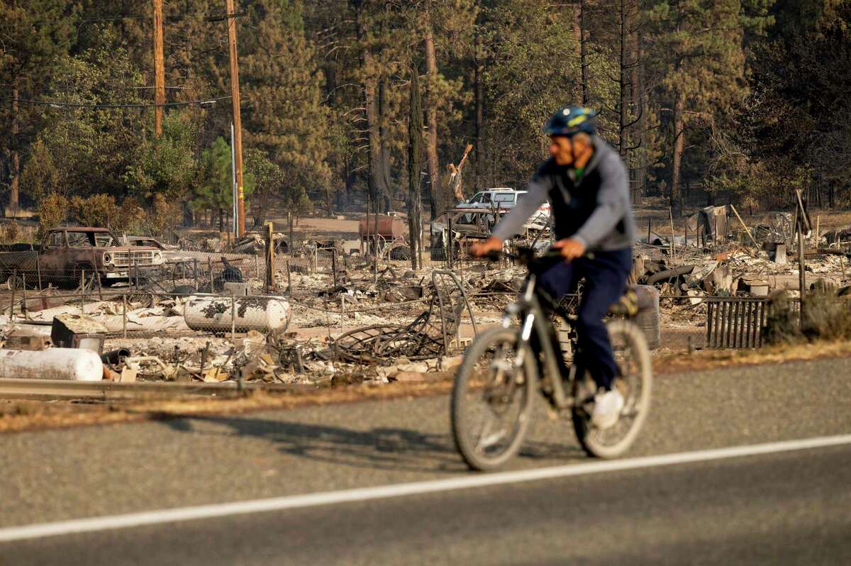 A bicyclist passes Wakefield Ave. homes destroyed by the Mill Fire on Saturday, Sept. 3, 2022, in Weed, Calif.