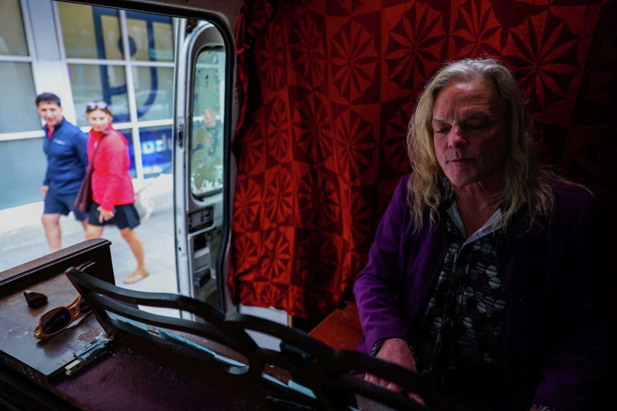 Pedestrians pass by a performer known as Mr. Brandy while he plays piano inside his live-in van at the corner of Haight and Cole in San Francisco. The musician, 62, has been playing in the Haight Ashbury community for six years. “I’m mostly playing my own stuff, but I play a few covers,” he said.