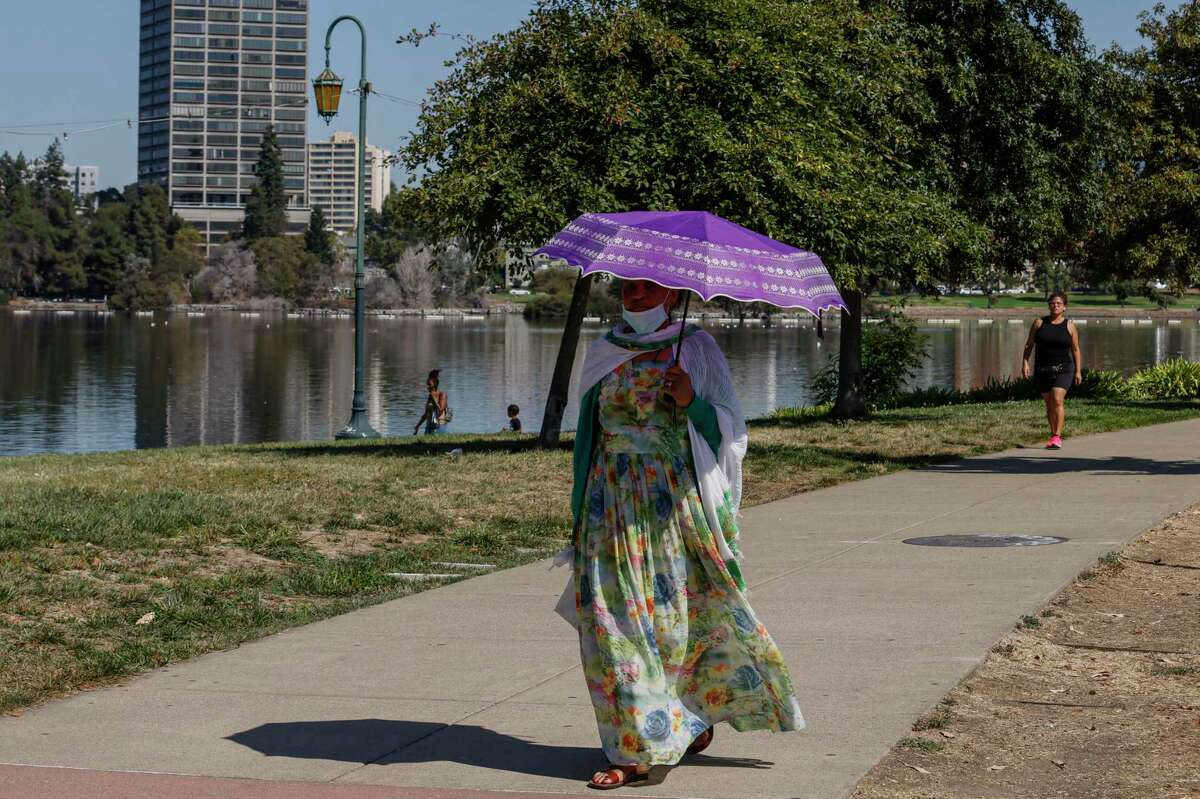 2022年9月5日，周一，在加利福尼亚州奥克兰的梅里特湖，一名男子用伞遮挡正午的阳光。高温警告和警告已经延长到周四。