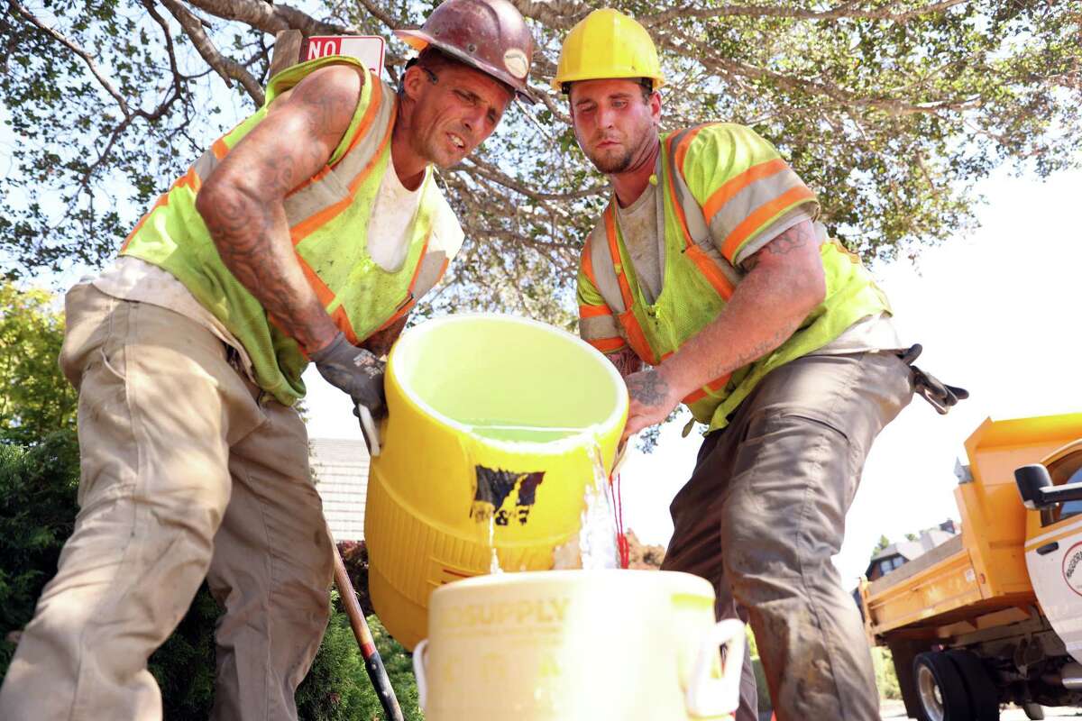 As temperatures hover around 100 degrees, Maggiora & Ghilotti’s Sal Bordessa and Mathew Hamilton fill up a water bucket while working on a water main replacement project on E. Blithedale Avenue in Mill Valley, Calif., on Tuesday, September 6, 2022.