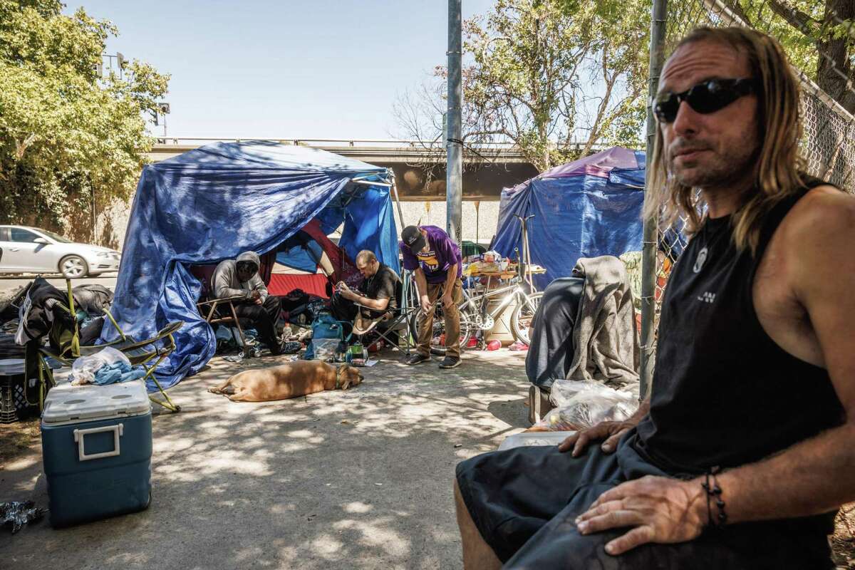 People hang out on a sidewalk in Sacramento, Calif., on Wednesday, Aug. 24, 2022. A citywide ballot measure calling for more homeless shelters and enforcement of unhoused people has revived the debate about the most effective way to treat homelessness — with temporary shelter or permanent housing.