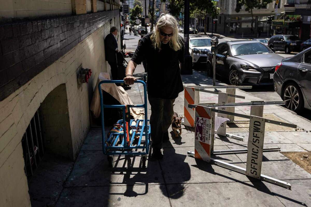 Wes Magnenat, with dog Meme, pushes a cart through the Tenderloin neighborhood while shuttling belongings from his room at the Crosby Hotel to a storage unit.