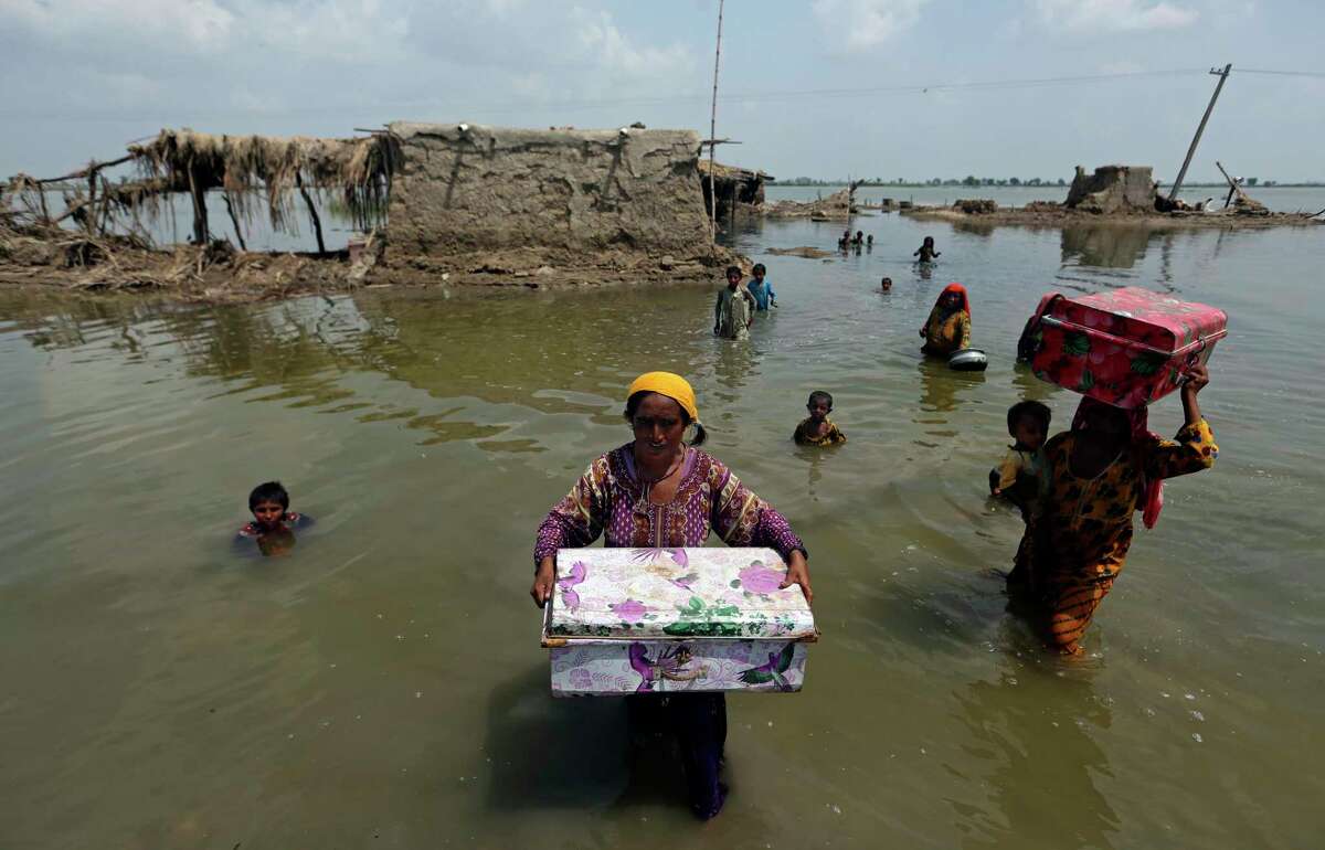 Women carry belongings salvaged from their flooded home after monsoon rains, in the Qambar Shahdadkot district of Sindh Province, of Pakistan, Tuesday, Sept. 6, 2022. More than 1,300 people have been killed and millions have lost their homes in flooding caused by unusually heavy monsoon rains in Pakistan this year that many experts have blamed on climate change. (AP Photo/Fareed Khan)