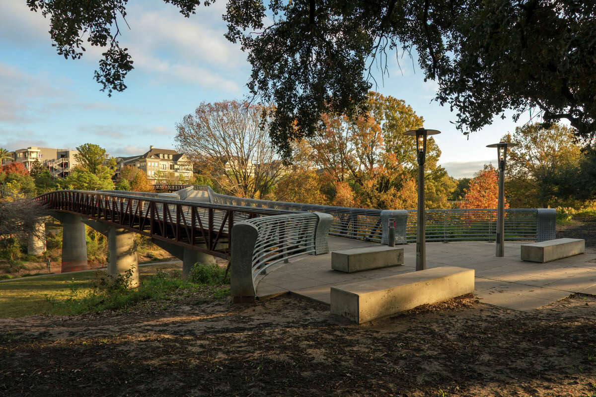 Early morning view of the entrance to pedestrian bridges over Buffalo Bayou in Houston's Buffalo Bayou Park with autumn colors in background.