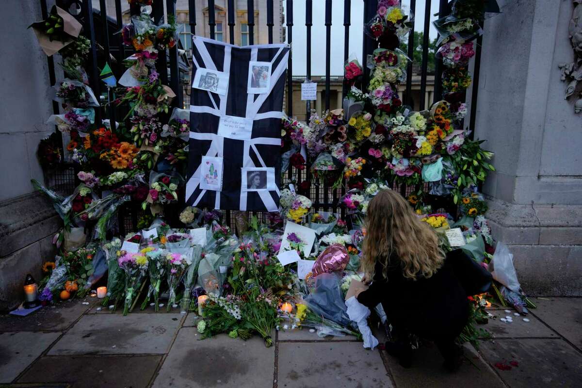A woman lays flowers and leaves a letter at the gates of Buckingham Palace in London on Friday, the day after the death of Queen Elizabeth II, Britain’s longest-reigning monarch.