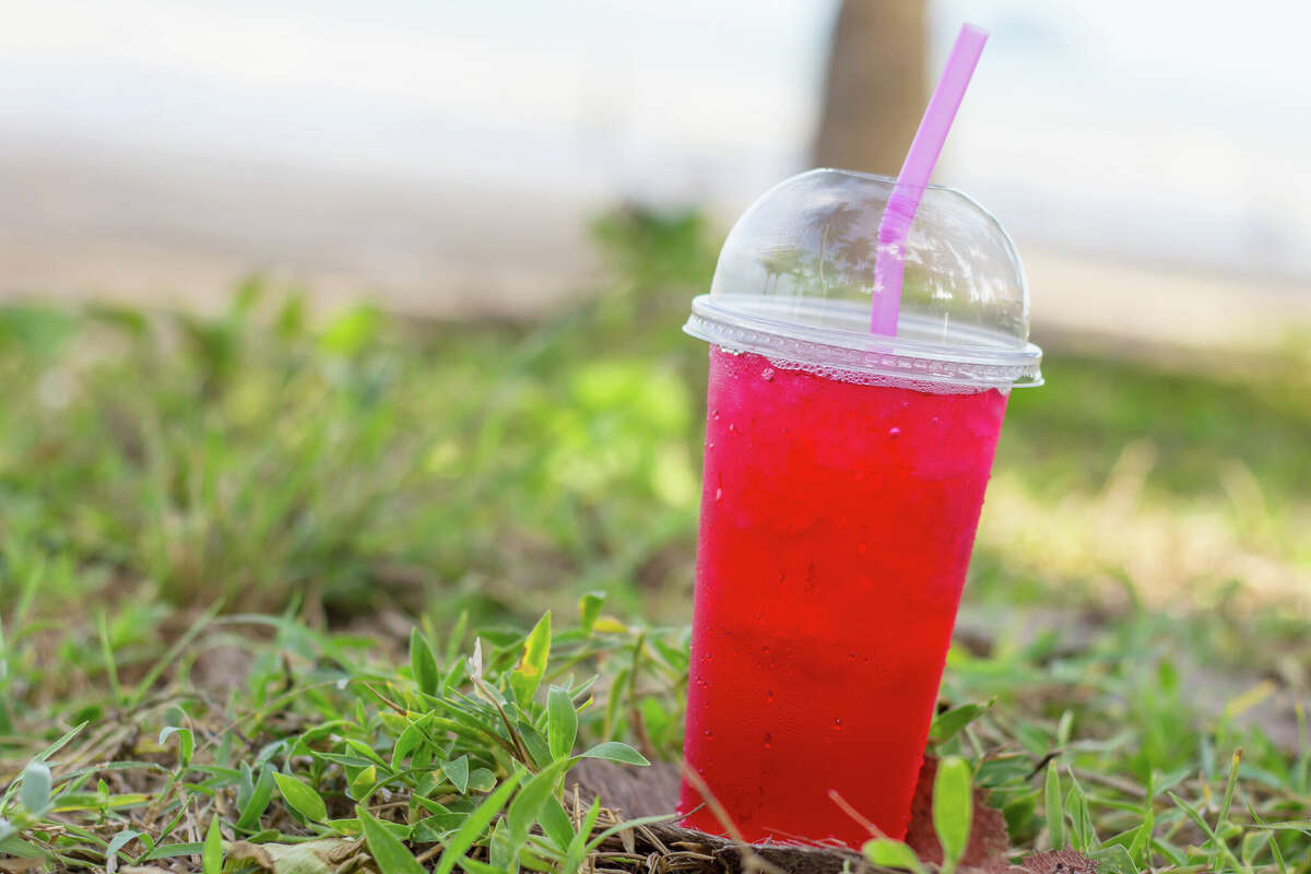 A cup filled with ice and soda is seen near the beach. Big Red, invented in San Antonio, can be used to make Raspas during hot days.