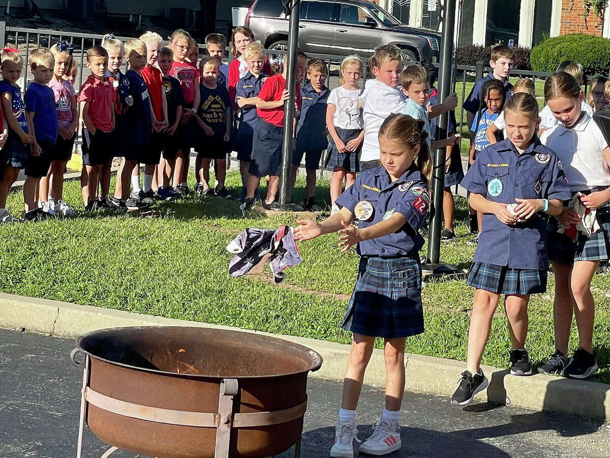 St. Boniface Catholic School student Nora Cullen tosses a piece of a retired flag on the prepared fire Friday at school during a ceremony to retire and honor United States flags.
