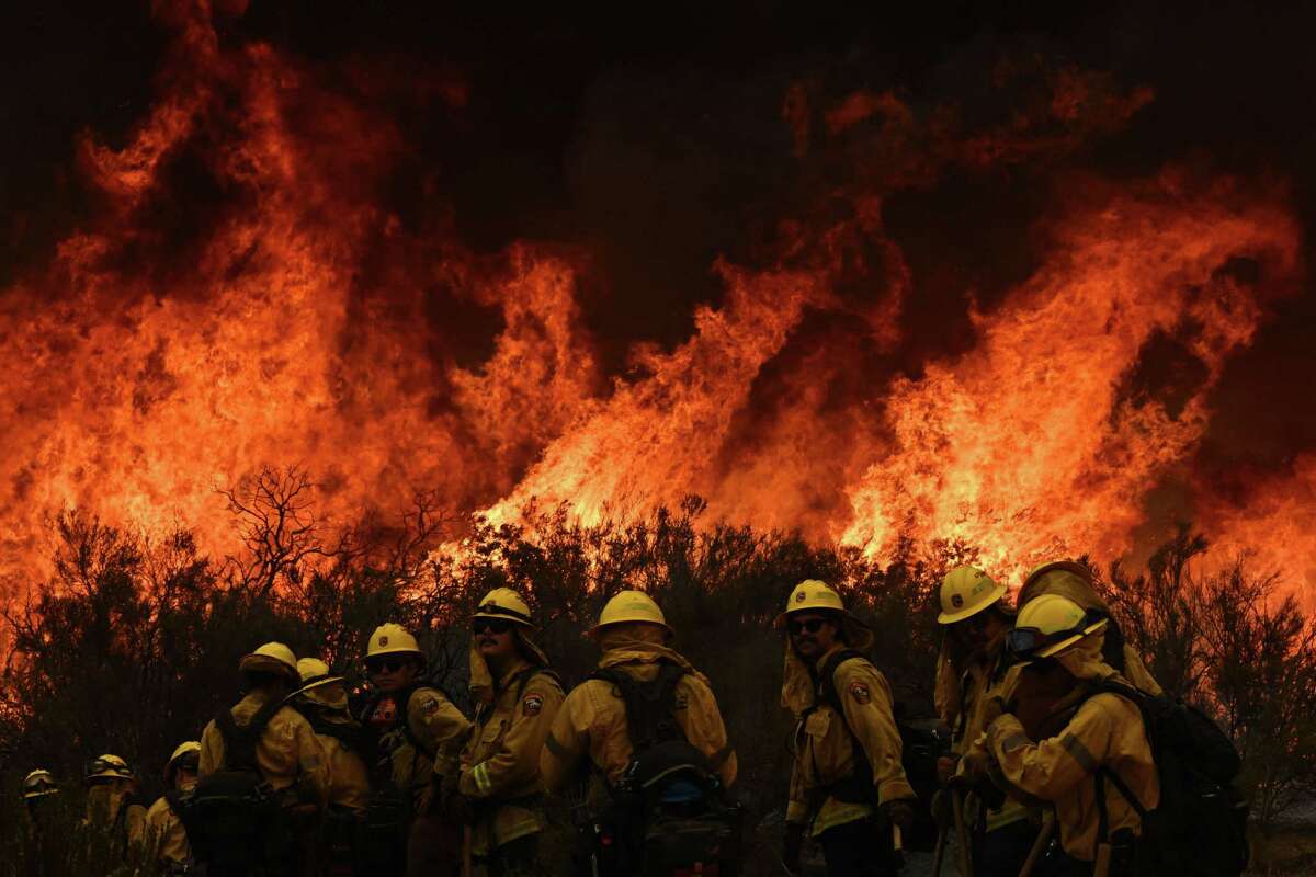 CalFire firefighters turn away from the fire to watch for any stray embers during a firing operation to build a line to contain the Fairview Fire near Hemet, California, on September 8, 2022. 
