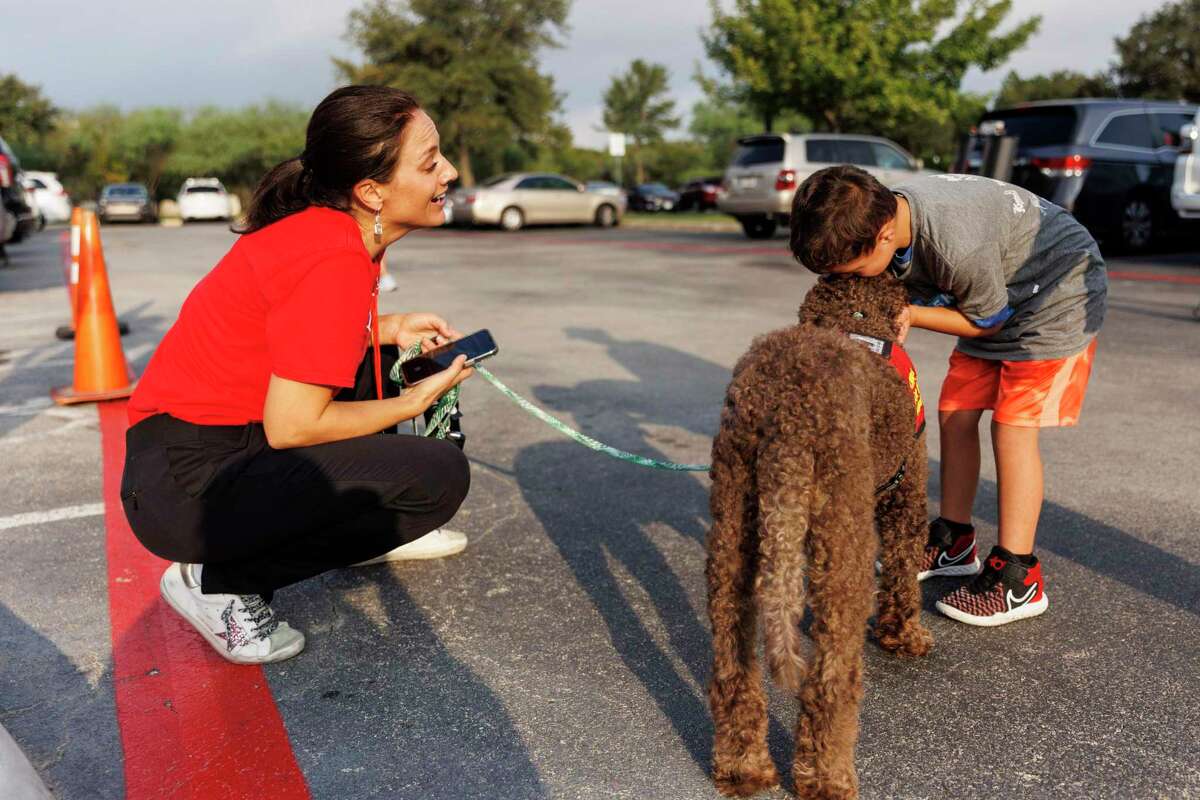 Canines For Christ volunteer Ayla Rahmberg reacts as she watches a child give her therapy dog Zoey a kiss after participating in a local 5K race in San Antonio on Saturday. The organization has supplied therapy dogs to kids in Uvalde all summer. “Even if the kids don’t want to talk, they can pet them, or lay on them, or hug them,” Rahmberg said.