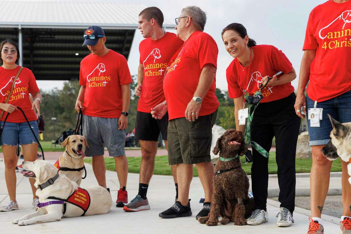 Canines For Christ volunteers and their therapy dogs, including Ayla Rahmberg with Zoey, right, prepare to take a group picture after participating in a 5K race in San Antonio on Saturday. The organization has supplied therapy dogs to kids in Uvalde all summer. Its mission is to go out into the community to “spread God's message of love, hope, kindness, and compassion.”