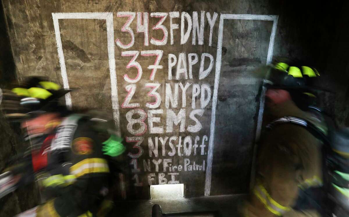 Firefighters walk past a graphic with the list of emergency workers who died in the Sept. 11 terrorist attacks on the World Trade Center towers in 2001as firefighters from around Texas take part in a 9/11 memorial climb at the Conroe Fire Training Facility, Saturday, Sept. 10, 2022, in Conroe. Participants climbed 60 flights of stairs to honor the 343 firefighters who died and thousand of emergency workers still affected.