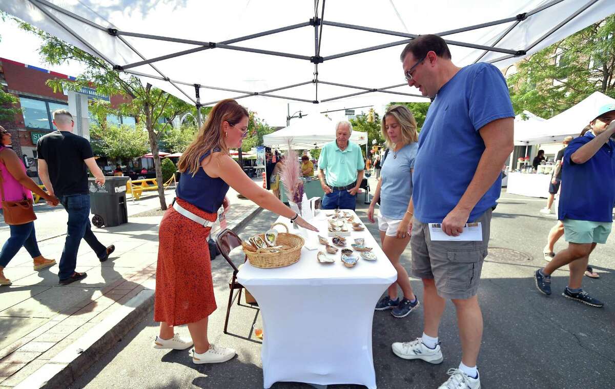 Christina Callahan, of The Rustic Mermaid, shows customers works of art she creates using clam and oyster shells, during the annual Arts & Crafts on Bedford event on Bedford Street in downtown Stamford, Conn., on Saturday September 10, 2022. Arts & Crafts on Bedford brings juried artisans from throughout the Northeast who will display and sell juried works including ceramics, fiber arts, fine art, jewelry, metal, photography, painting, wood and more. Arts & Crafts on Bedford is presented by Stamford Downtown Special Services District and sponsored by 95.9 The Fox, Star 99.9, WEBE 108 and Happyhaha.com Photography.