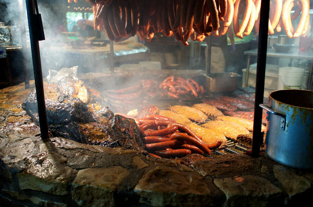 Meats and sausages cook over a large barbecue pit. 