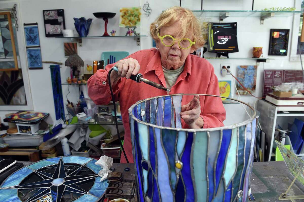 Jayne Crowley of J.C. ArtGlass Designs solders at piece of stained glass onto a lampshade at her studio in Branford.