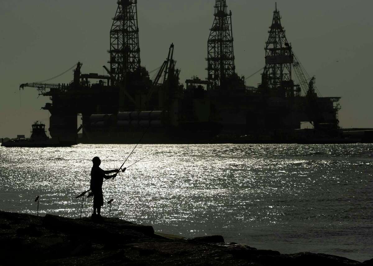FILE - A man wears a face mark as he fishes near docked oil drilling platforms on May 8, 2020, in Port Aransas, Texas. The U.S. government has accepted nearly $190 million in bids from an offshore oil and gas lease sale that was held nearly a year ago but rejected by a federal judge, the Bureau of Ocean Energy Management said Wednesday, Sept. 14, 2022.