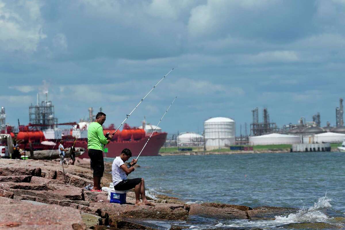 Fishermen sit on the Quintana Beach jetty waiting to catch fish, Sunday, Aug. 28, 2022, in Quintana. In the background is liquefied natural gas plants, Sunday, Aug. 28, 2022, in Quintana.