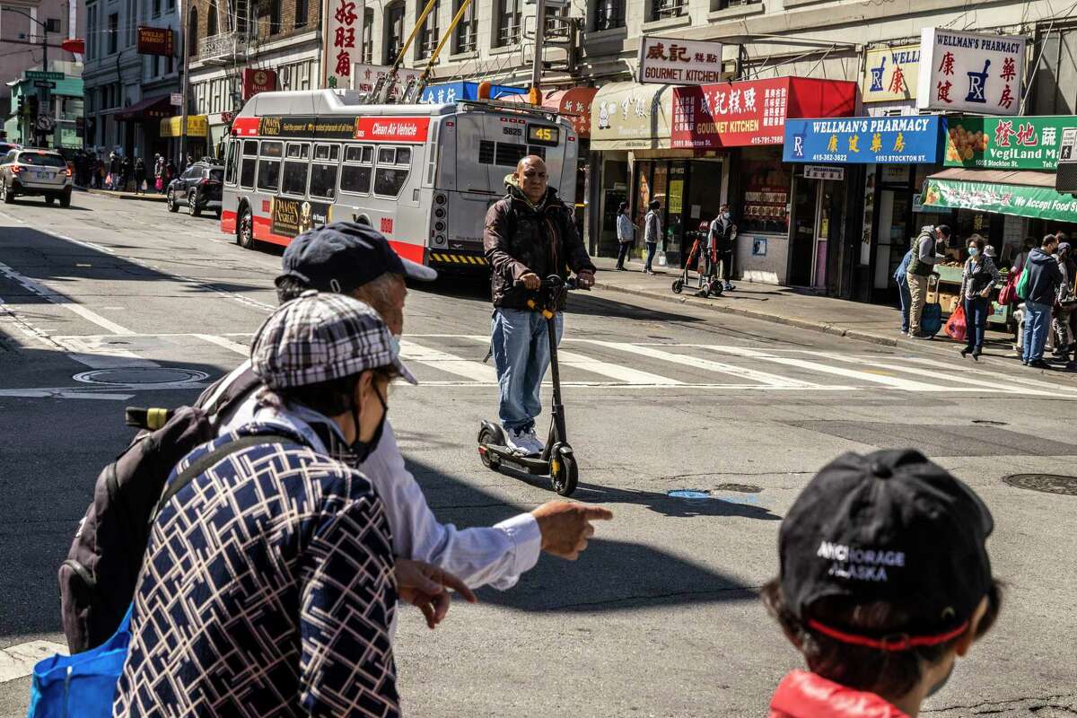 一名男子骑着摩托车沿着旧金山唐人街附近的斯托克顿街行驶。