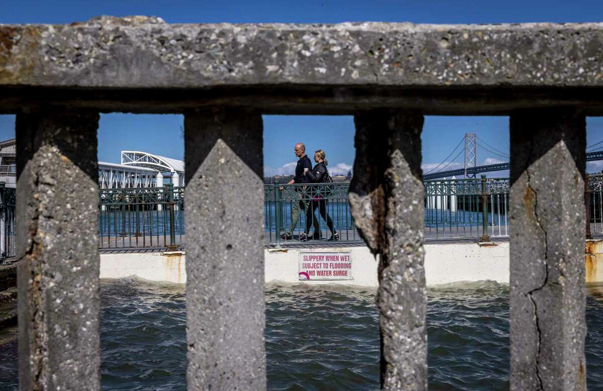 两个人从14号码头走出来，穿过旧金山英巴卡德罗海堤上破损的扶手。由于海水和岁月的影响，墙体和栏杆的构件已经开始变质。