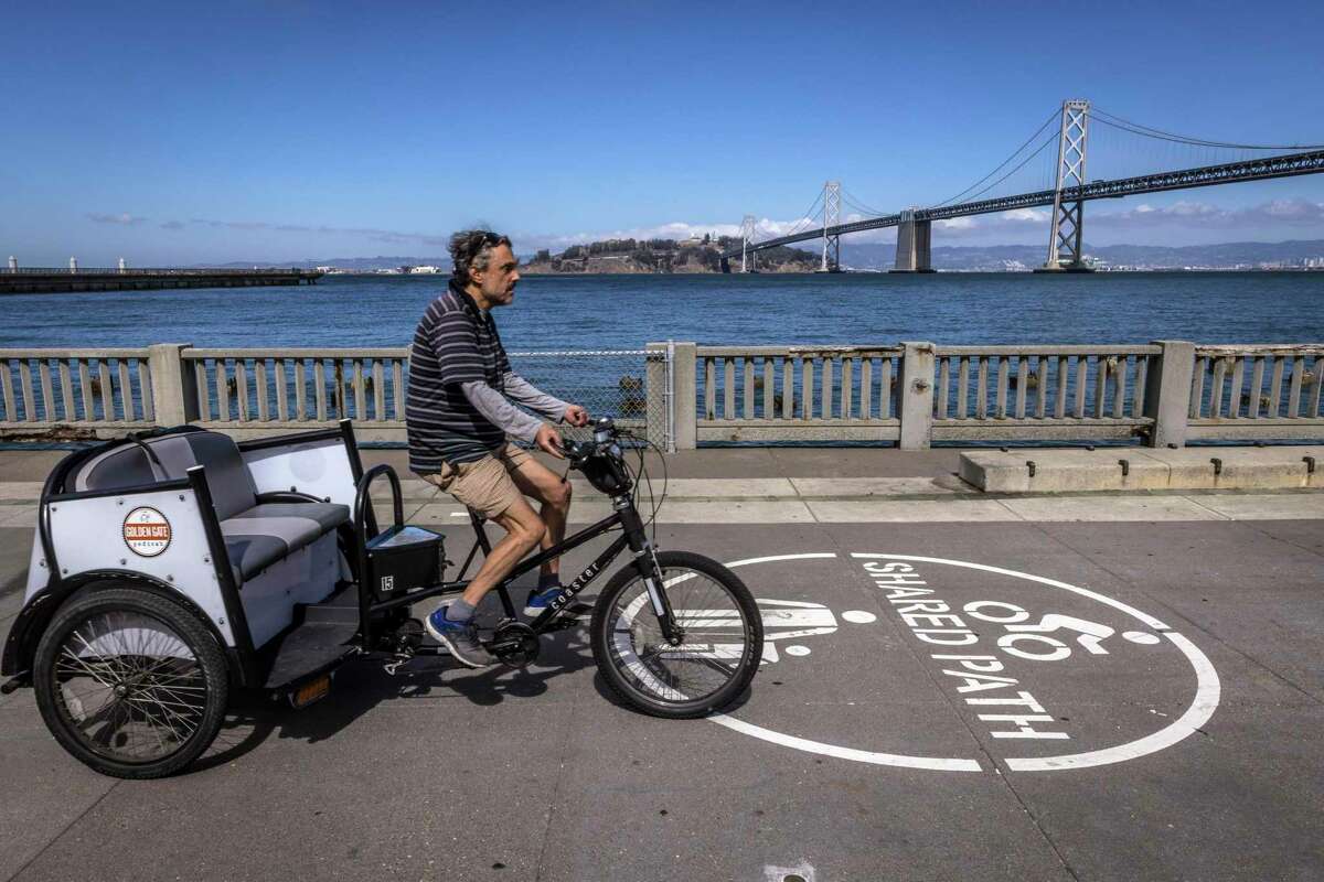 A pedicab passes by a repaired handrail at the sea wall along the Embarcadero in San Francisco.