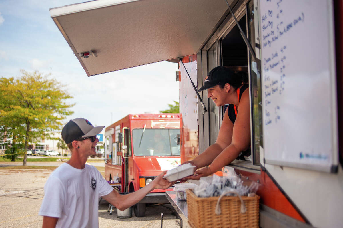 Midland resident Travis Phipps (left) receives food from Tina Shankel of Bigshow's Crazy Idea food truck during the Midland County Crime Stoppers Fundraiser on Sept. 16, 2022 in a parking lot by Midland Mall.