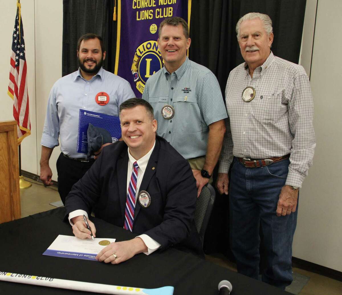 It’s all in the Family - Conroe Noon Lions Club President Warner Phelps (seated) make’s it official by signing the new member certificate of Nathan Vrazel (back left) as the third member of the Brennan clan to join the club. Nathan is the son-in-law to Bobby Brennan (back center) and grandson-in-law to Pat Brennan (back right).